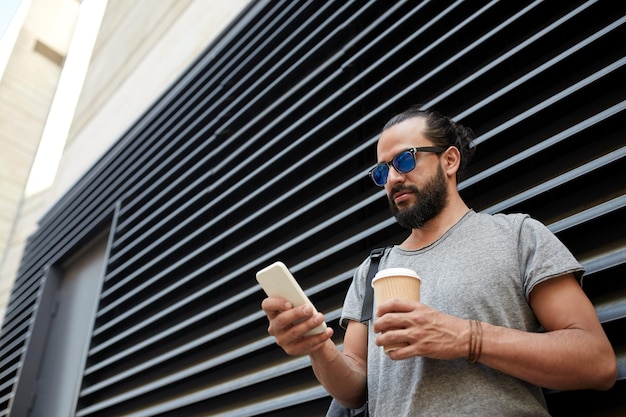 travel, tourism, communication, technology and people concept - man with backpack and coffee cup texting on smartphone on city street