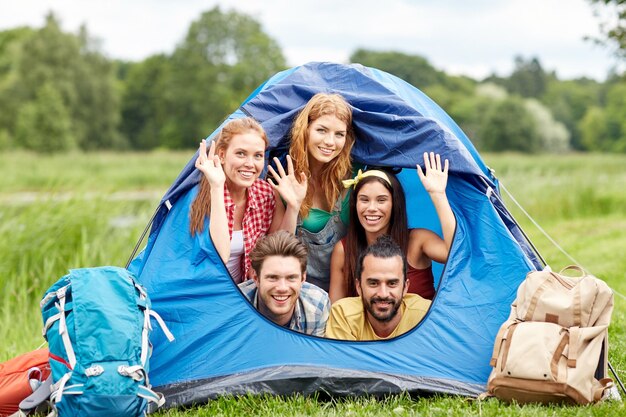 travel, tourism, hike, equipment and people concept - group of happy friends with backpacks in tent at camping