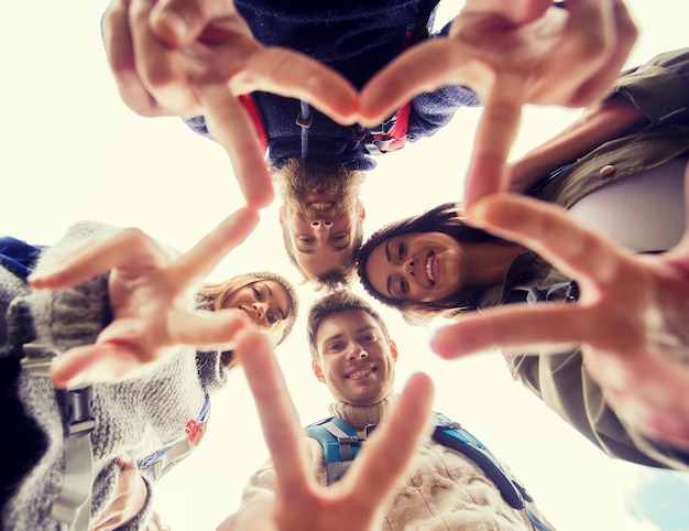 travel, tourism, hike, gesture and people concept - group of smiling friends with backpacks standing in circle and showing victory sign outdoors