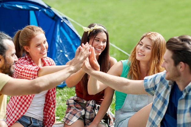 Photo travel, tourism, hike and people concept - group of happy friends with tent making high five at camping