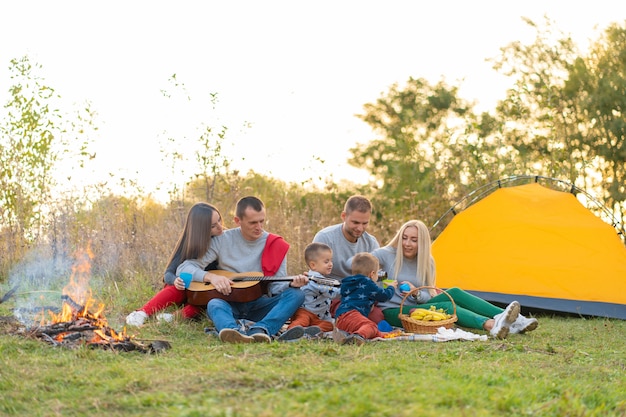 Travel, tourism, hike, picnic and people concept - group of happy friends with tent and drinks playing guitar at camping