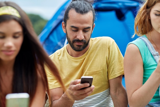 Concetto di viaggio, turismo, escursione, tecnologia e persone - gruppo di amici con smartphone e tenda in campeggio