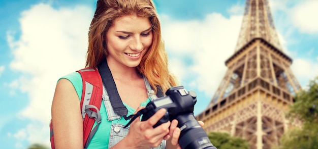 Photo travel, tourism and people concept - happy young woman with backpack and camera photographing over eiffel tower background