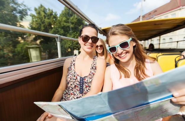 Photo travel, tourism, summer vacation, sightseeing and people concept - group of smiling teenage friends in sunglasses with map traveling by tour bus