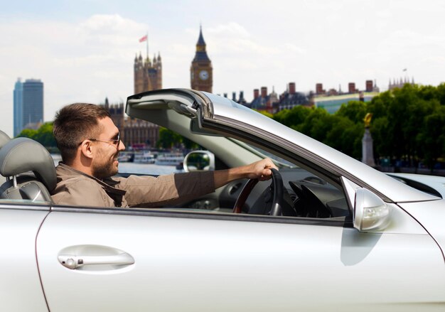 travel, tourism, transport, leisure and people concept - happy man near cabriolet car over london city background