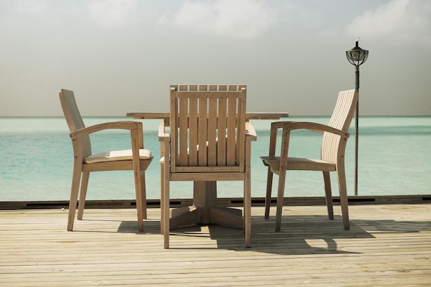 여행, 관광, 휴가 및 여름 휴가 개념 - 바다 배경 위에 테이블과 의자가 있는 야외 레스토랑 목재 테라스