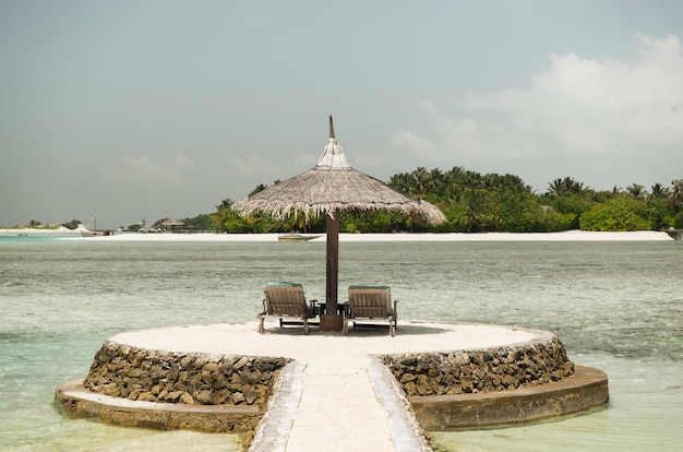 travel, tourism, vacation and summer holidays concept - palapa and sunbeds over sea and sky on maldives beach