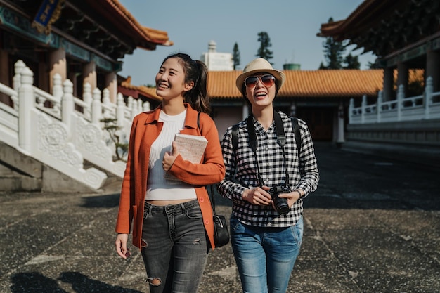 Travel tourist frienship. two smiling girls backpackers walking in chinese confucius temple in beijing china. Beautiful women in stylish clothes sightseeing history attractions look architecture