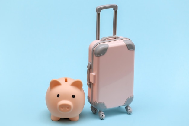 Travel or trip concept. Mini plastic travel suitcase and piggy bank on blue background. Minimal style