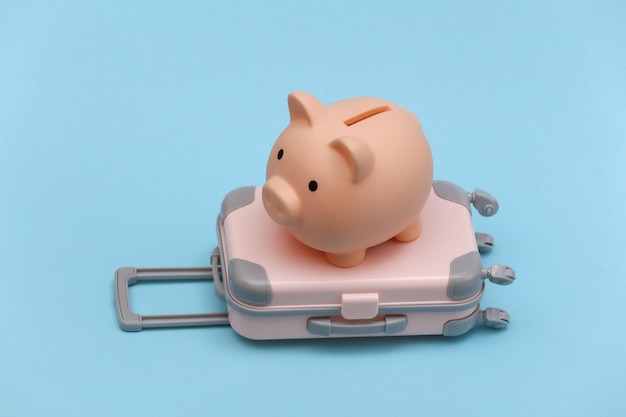 Travel or trip concept. Mini plastic travel suitcase and piggy bank on blue background. Minimal style