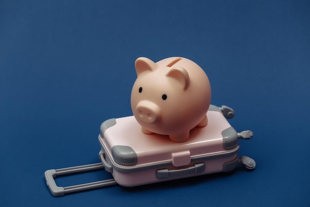 Travel or trip concept. Mini plastic travel suitcase, piggy bank on classic blue background. Color 2020