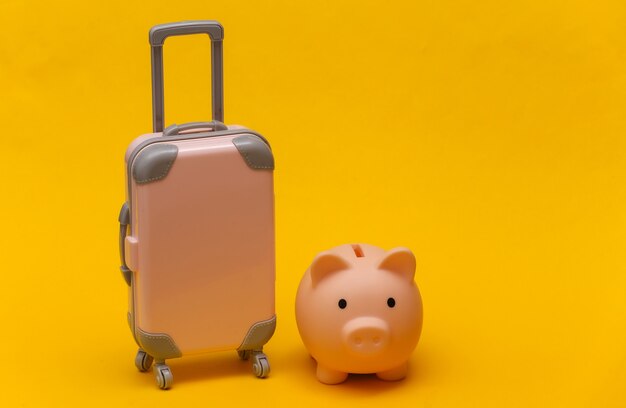 Travel or trip concept. Mini plastic travel suitcase and piggy bank on yellow background. Minimal style