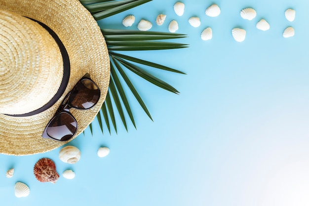 Путешествие, концепция отпуска. Шляпа с морскими раковинами, пальмовым листом и очками на синем фоне.