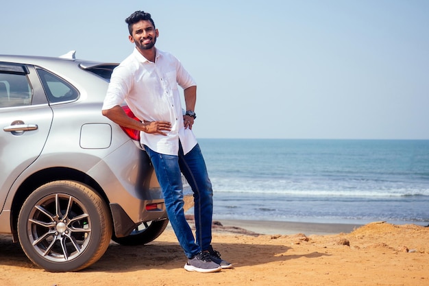 Travel vacation happy indian man in white shirt collar buying new car and showing the key, sitting in car on beach sea india octan Goa .a trip to the beach in car