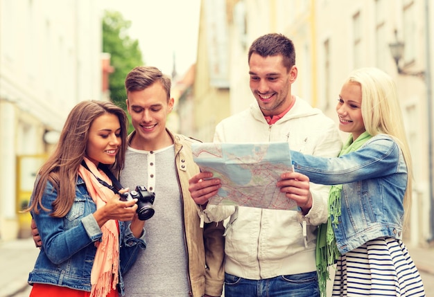 travel, vacation, technology and friendship concept - group of smiling friends with map and photocamera exploring city