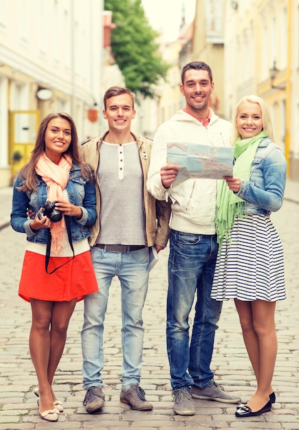 travel, vacation, technology and friendship concept - group of smiling friends with map and photocamera exploring city