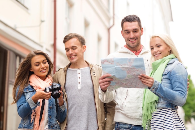 Concetto di viaggio, vacanza, tecnologia e amicizia - gruppo di amici sorridenti con mappa e fotocamera che esplorano la città