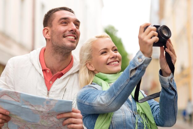 travel, vacation, technology and friendship concept - smiling couple with map and photocamera exploring city