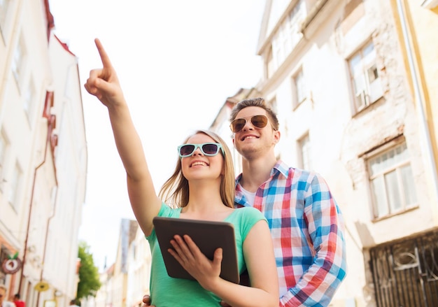 Photo travel, vacation, technology and friendship concept - smiling couple with tablet pc computer in city