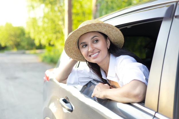 旅行休暇 帽子をかぶった若い美しい女性が車の中に座り、遠くを見て微笑む