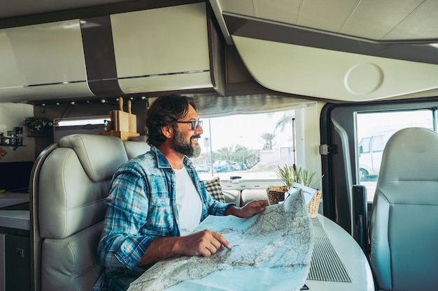 Travel with vehicle camper concept people lifestyle One man smiling and choosing on road map next destination Tourism with van Alternative home and vanlife style Happy adult on vacation motorhome