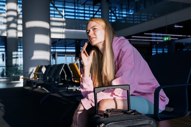 Travel without borders a young woman with a pink hoodie is
talking on the phone sitting in the lobby of the airport at the
international airport