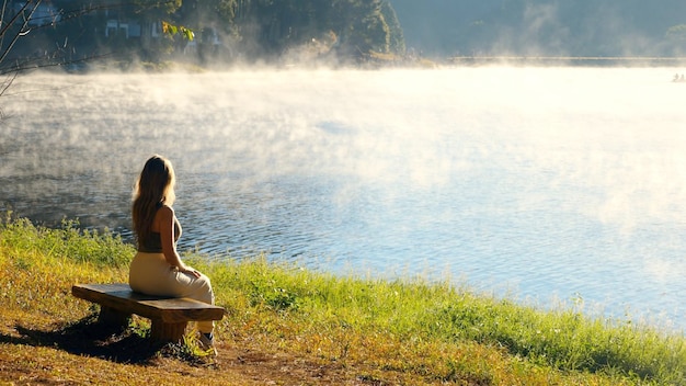 Travel woman relax on nature near misty lake female traveler sitting on bench