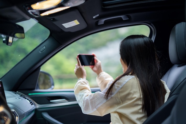 旅行中の女性が携帯電話を使って写真を撮り車の中に座ります