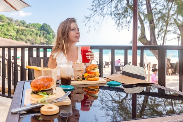 屋外カフェでファーストフードのハンバーガーコーヒーとジュースの飲み物を持つ旅行の女性