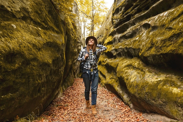 Travel young woman wearing brown hat plaid shirt jeans and\
brown boots with backpack ready to taking picture of wonderful\
canyon with moss on rocks after hiking travelling concept