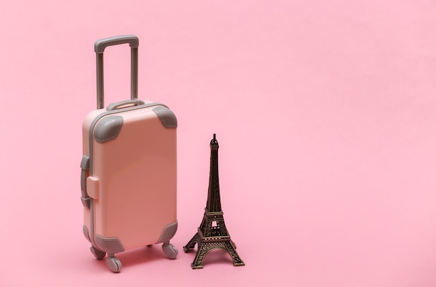 Traveled to Paris. Mini plastic travel suitcase and statuette of the Eiffel Tower on pink background.