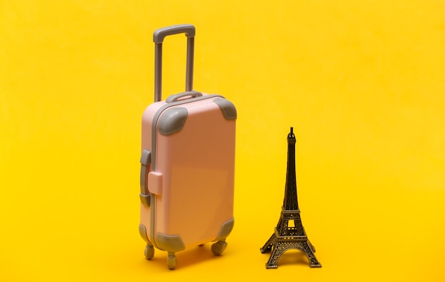 Traveled to Paris. Mini plastic travel suitcase and statuette of the Eiffel Tower on yellow background.