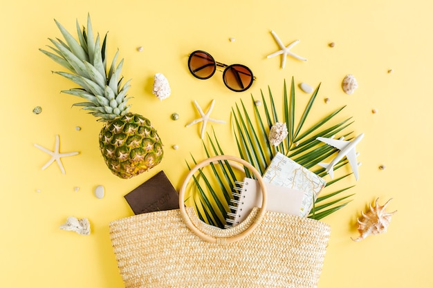 Концепция аксессуаров для путешественников на желтом фоне. Эко-сумка из ротанга, модель самолета, солнцезащитные очки, ананас и тропический пальмовый лист.