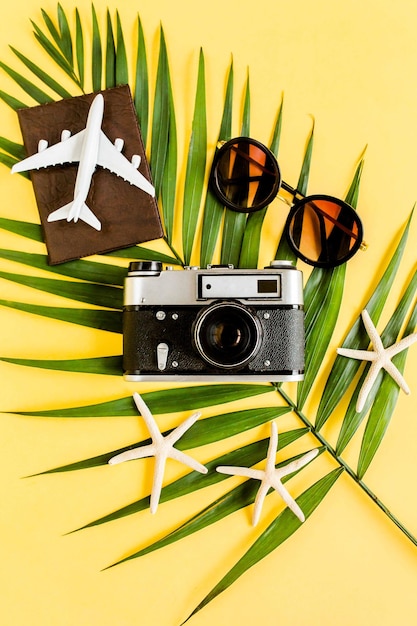 Foto concetto di accessori per viaggiatori su sfondo giallo modello di fotocamera retrò occhiali da sole aereo passaporto e foglia di palma tropicale sfondo estivo
