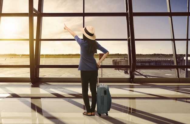 Foto donna asiatica del viaggiatore con la valigia che guarda tramonto attraverso la finestra