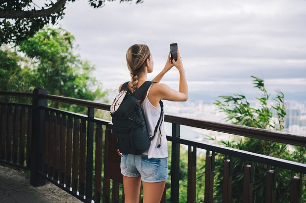 Traveler blonde backpacker woman walking taking photos from observation deck overlooking the downtown. Travel adventure in China, Tourist beautiful destination Asia, Summer holiday vacation trip