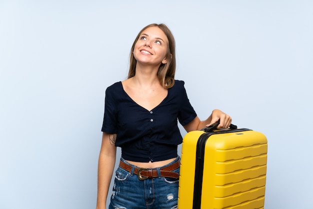 Donna bionda del viaggiatore con la valigia che cerca mentre sorridendo