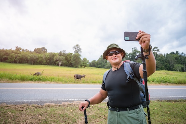 A traveler carrying a hiking backpack is watching deer grazing in the forest. Tourists take a selfie with deer grazing in a tropical forest in Khao Yai National Park, Thailand.