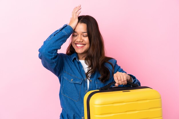 Traveler Colombian woman holding a suitcase over isolated pink wall has realized something and intending the solution