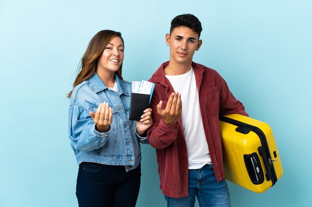 Traveler couple holding a suitcase on blue inviting to come with hand. Happy that you came