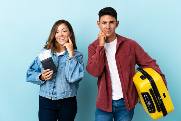 Traveler couple holding a suitcase on blue smiling with a sweet expression