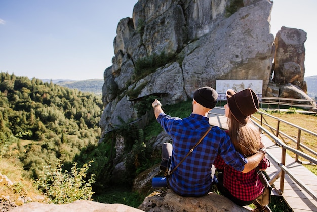 Photo a traveler couple sitting together on the rocks at the mountains over the blue sky background