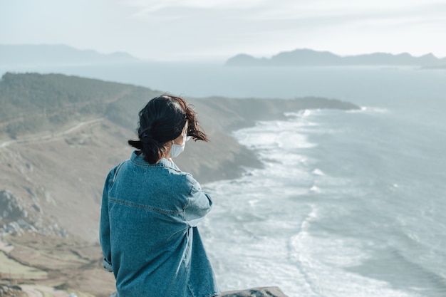 A traveler in front of the spanish wild coast wearing a face mask, wellness concept, life and freedom