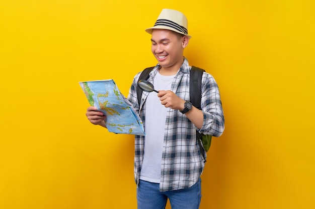 Traveler fun exploring tourist asian man in casual clothes hat hold city map look through magnifier loupe on yellow background passenger travel abroad weekends getaway air flight journey concept