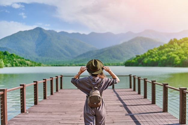 Traveler girl backpacker standing alone on pier and staring at lake and mountains