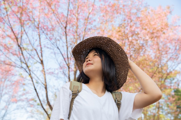 旅行者の女の子の帽子を押しながら桜の木を見て