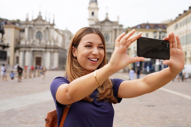 Photo traveler girl on landmark city square makes self portrait. young female tourist video calling and showing cityscape during her travel in europe.