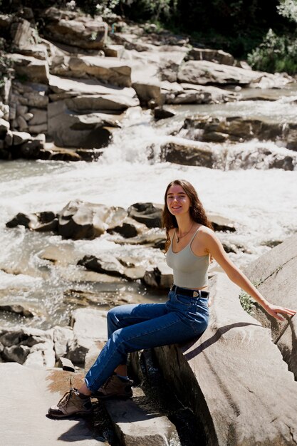 Traveler girl sitting on the rock near waterfall and looking toward.