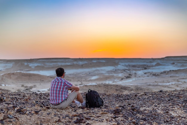 Traveler guy in a plaid shirt looks at the sunrise in a rocky area
