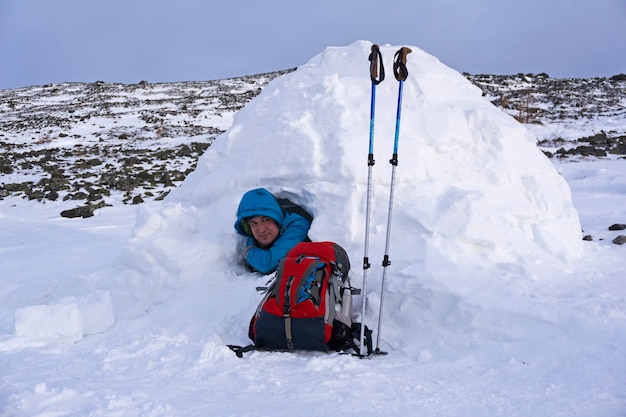 Traveler looks out of a snowy house igloo against a background of a winter mountain landscape